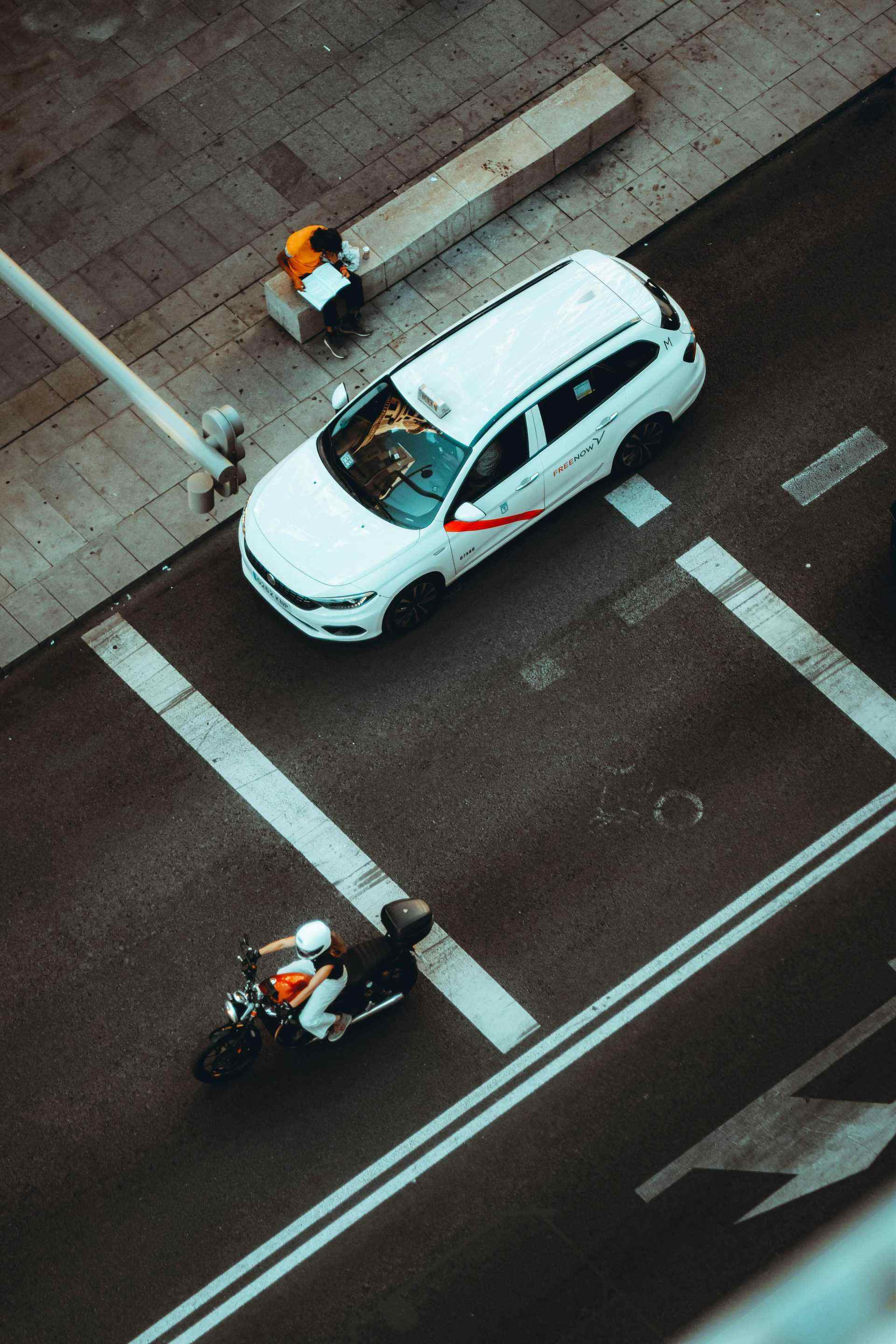 Un coche blanco circulando por una calle al lado de una motocicleta.